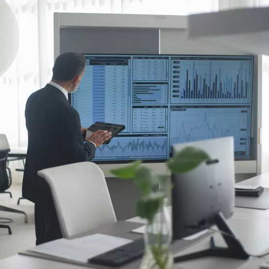 A man wearinga black  suit standing in front of a screen with financial figures on display