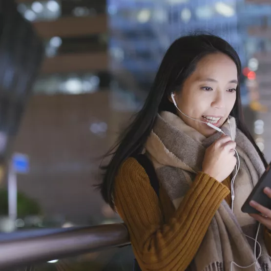An Asian woman staring into her phone at a train station