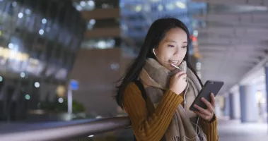 An Asian woman staring into her phone at a train station