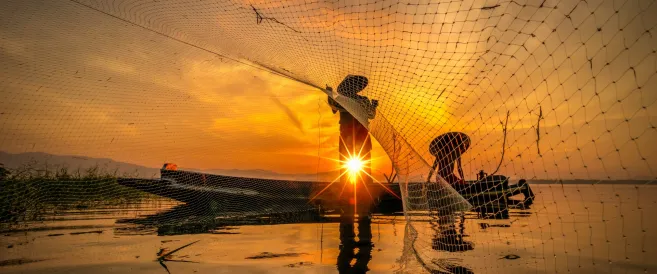 Image of two fishermen on a boat casting a net over the sea